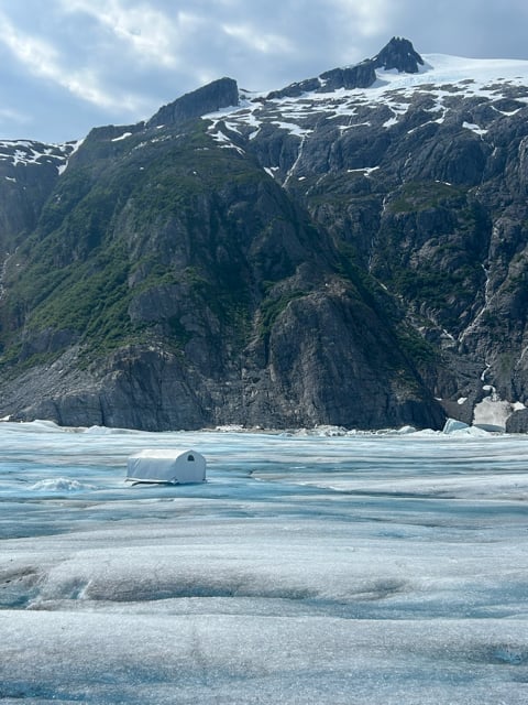 Blue glacier ice below snow-capped Alaska mountains