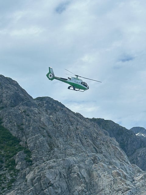 Helicopter flying beside steep Alaska cliffs